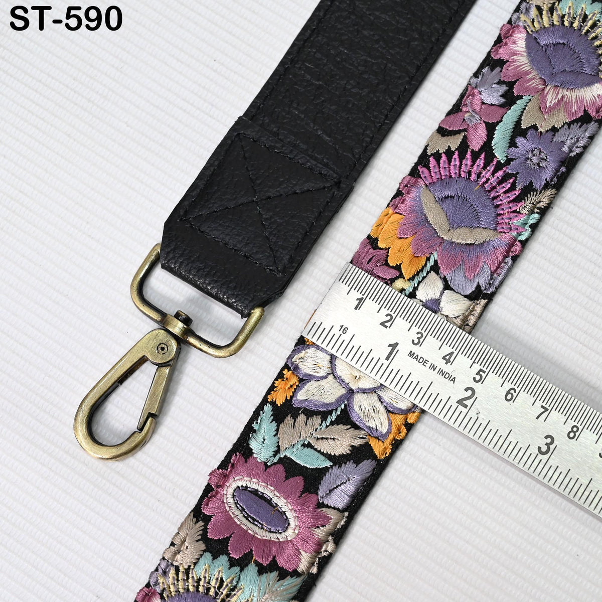 a black leather strap with a floral pattern and a gold-colored metal clasp, placed next to a ruler for size comparison.