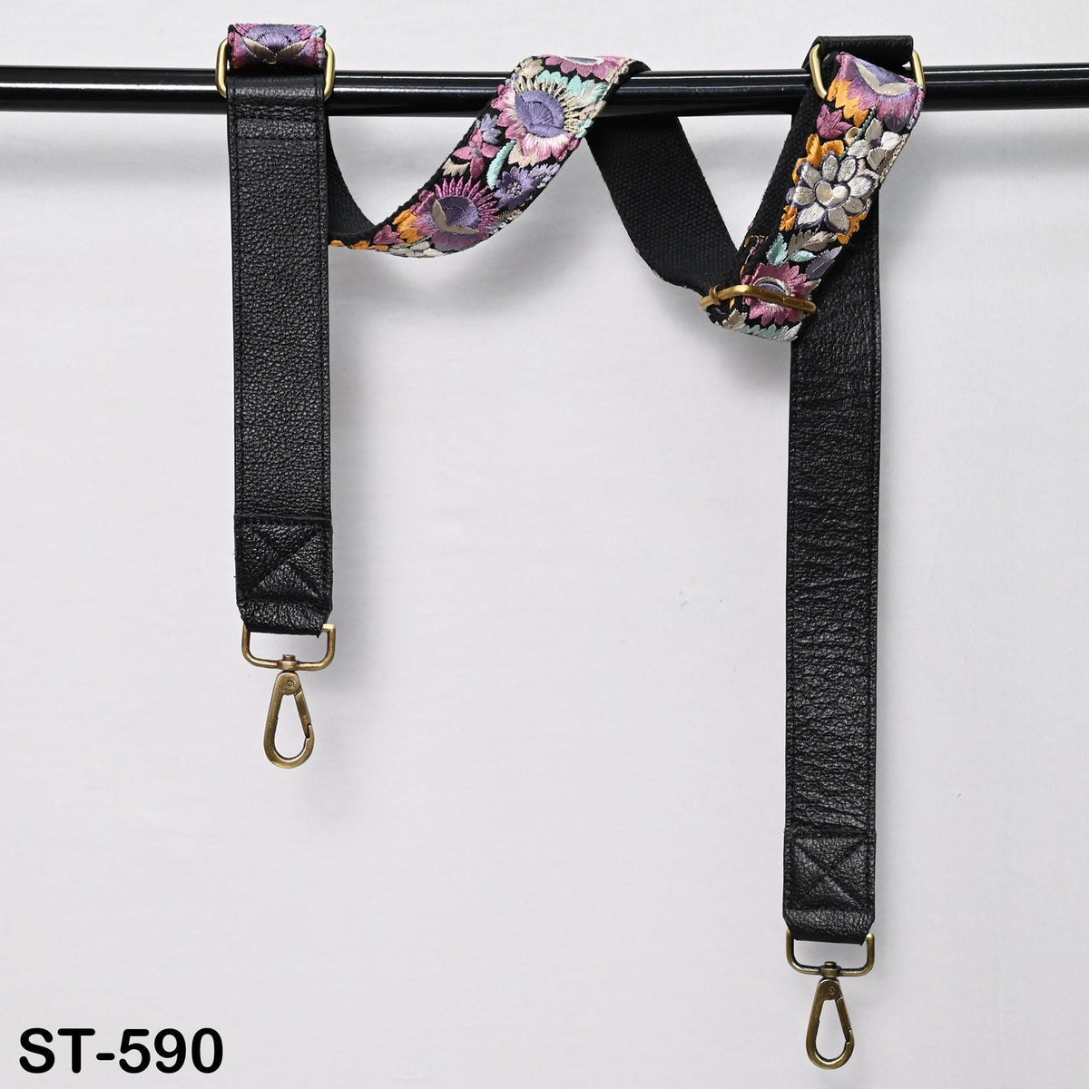 A pair of black leather straps with floral patterns, hanging from a black metal bar.