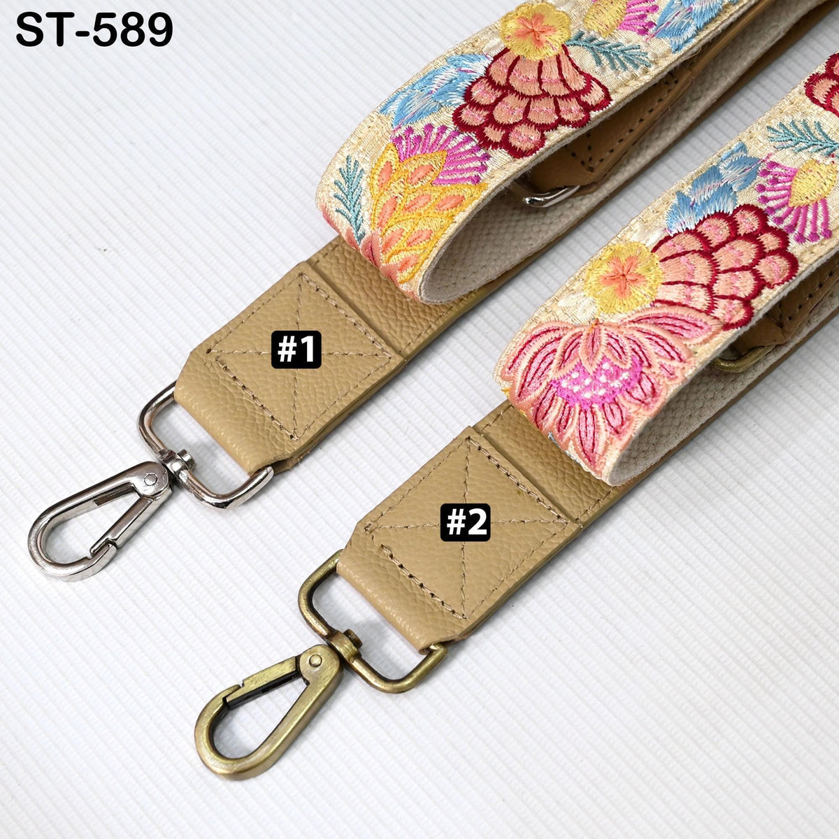 two beige straps with floral embroidery, each with a metal clasp and a metal loop. The straps appear to be made of leather and are displayed on a white surface.