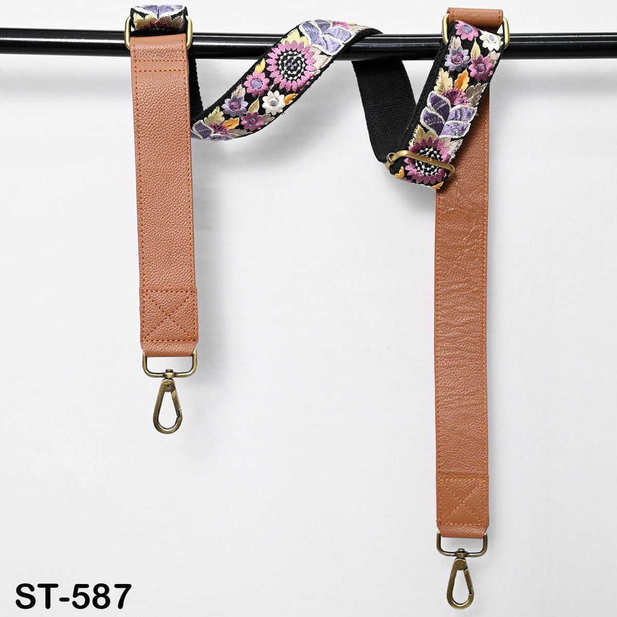 two leather straps with floral patterns hanging on a black bar.