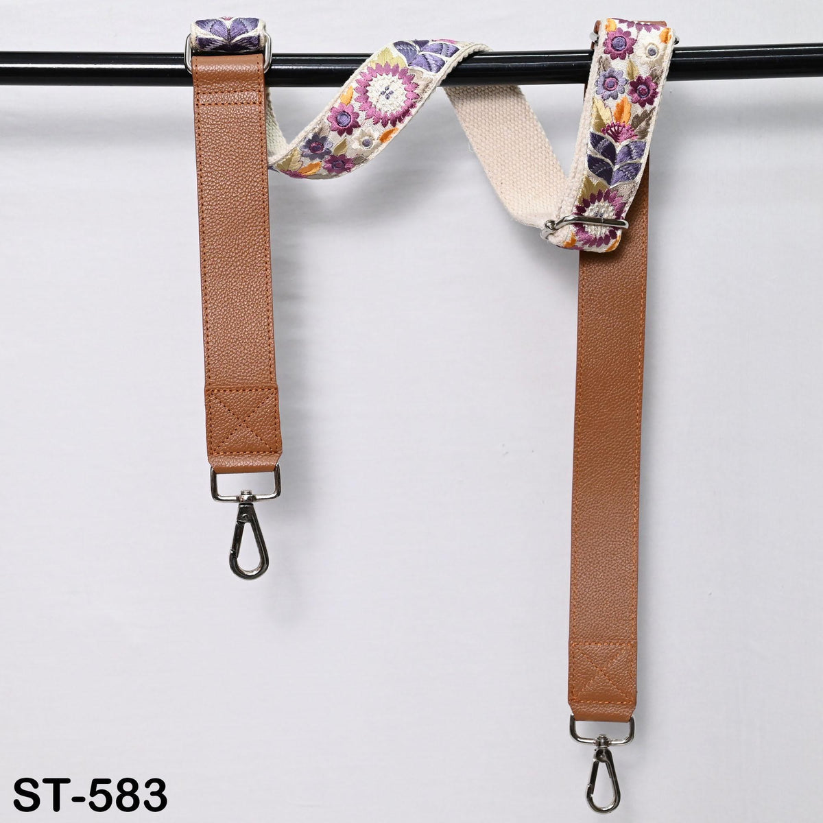 two brown leather straps with floral patterns hanging on a black pole.