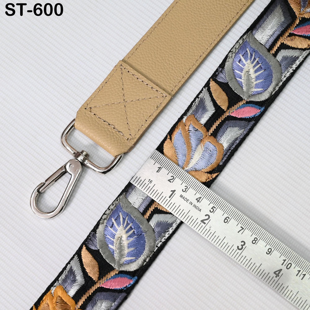 a beige strap with a floral pattern and a metal hook, along with a ruler for size comparison.