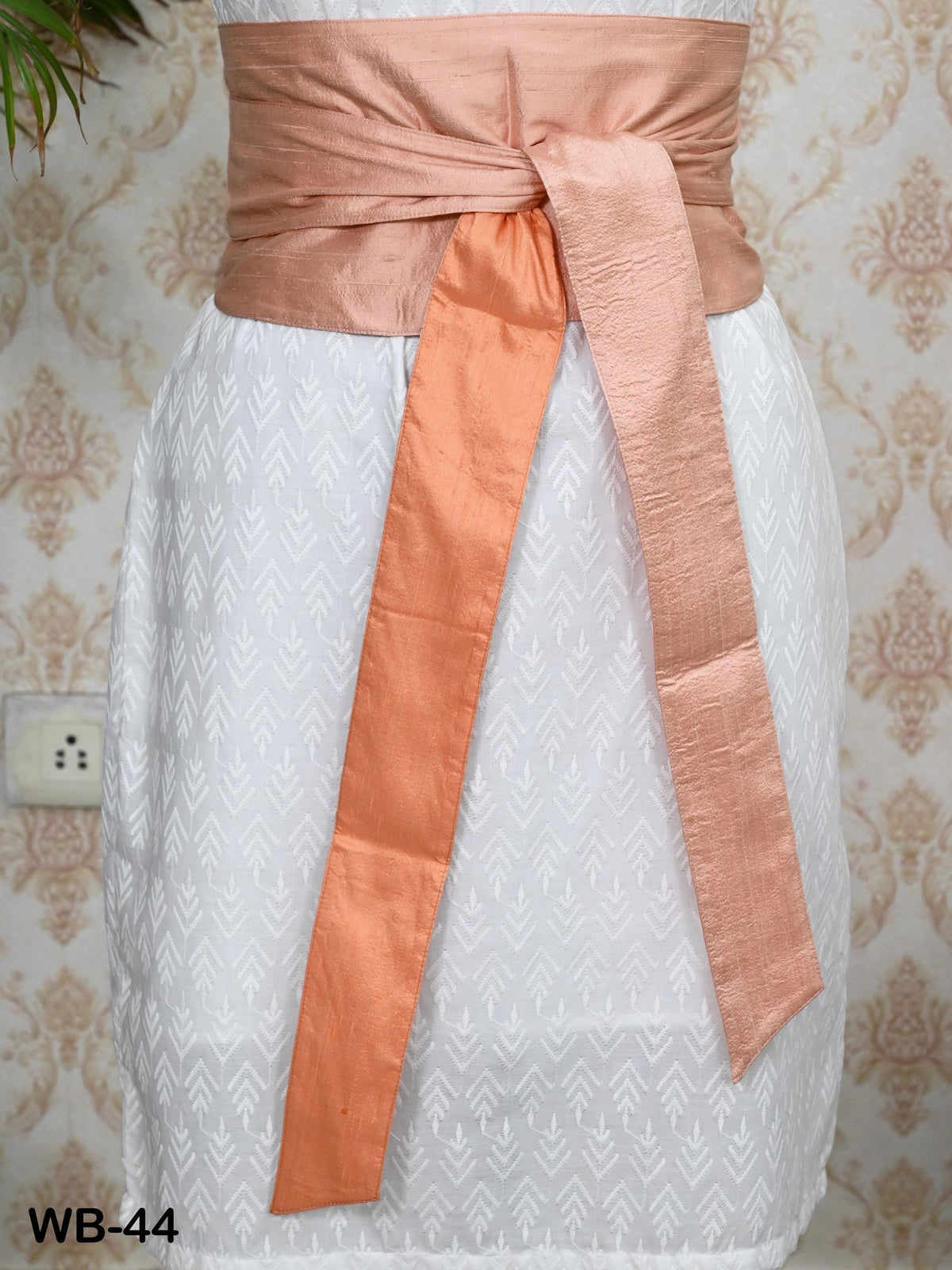 A white dress with a peach-colored sash tied around the waist.