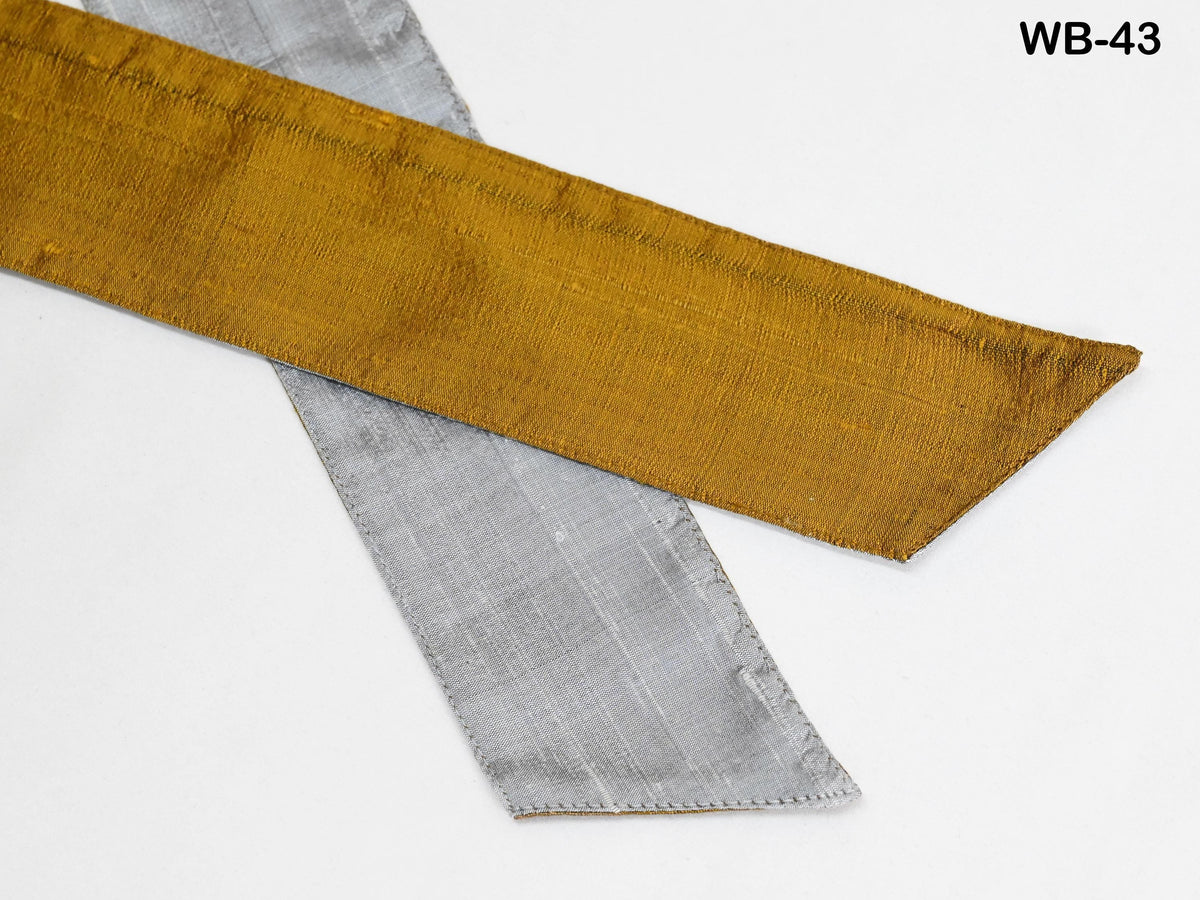a close-up view of a gold and silver ribbon or fabric, with the gold ribbon appearing to be slightly curled and overlapping the silver ribbon.