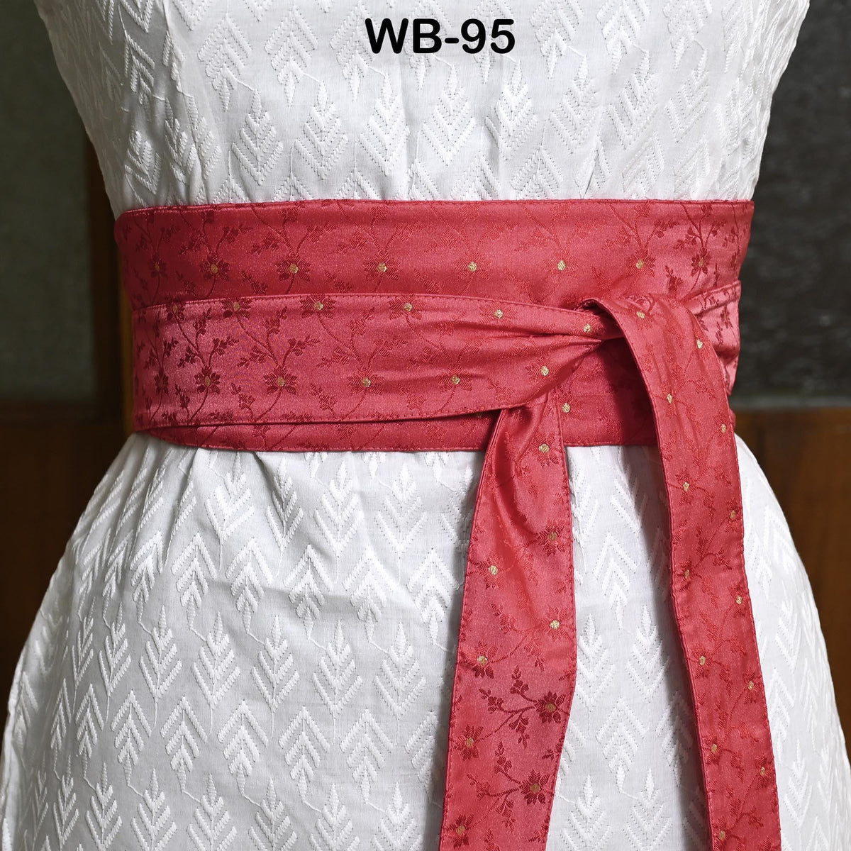 A close-up view of a red sash tied around a white dress, with a patterned fabric.