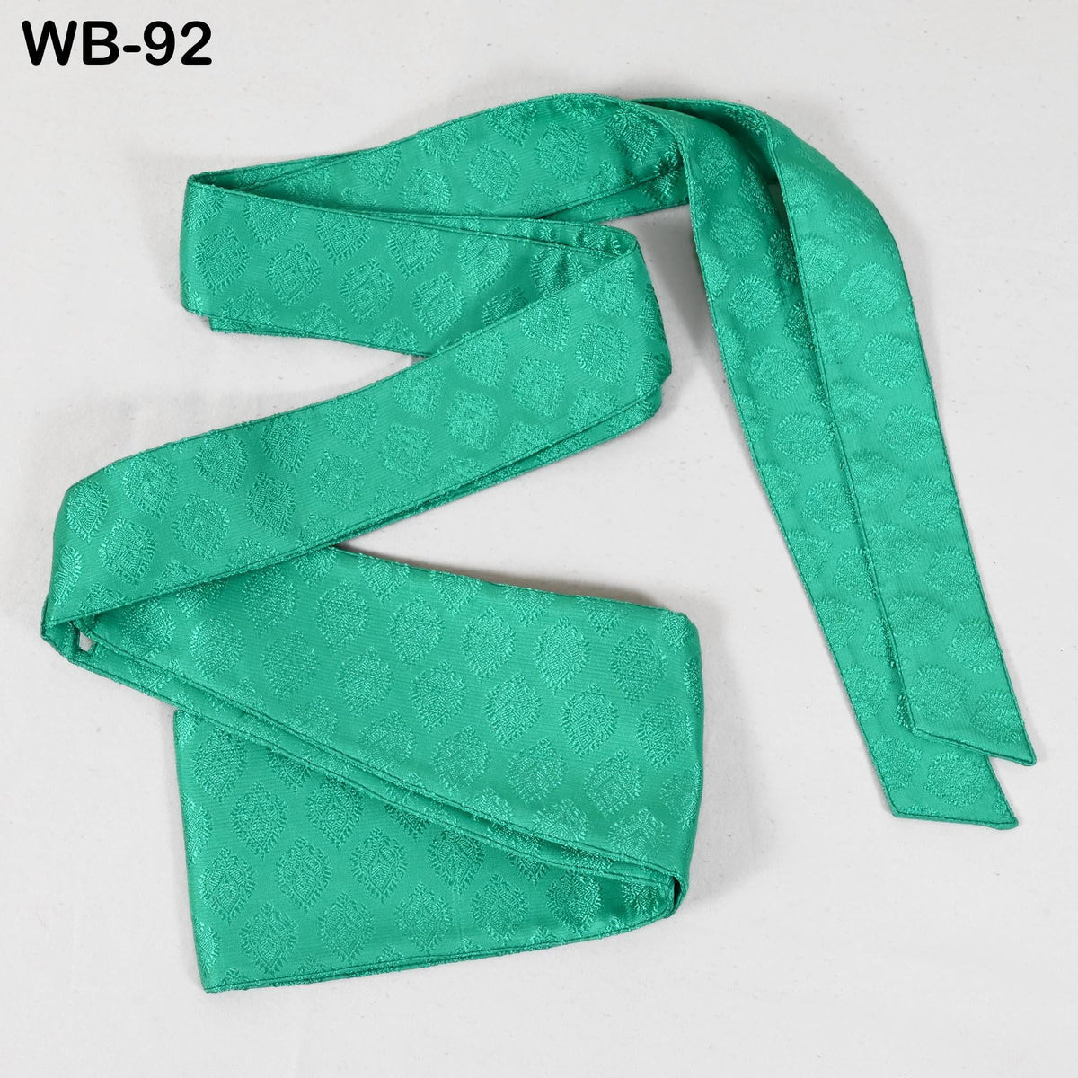 A green satin tie with a patterned design, lying on a white surface.