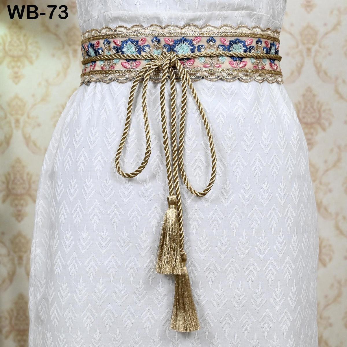 A close-up view of a white dress with a decorative belt featuring a floral pattern and gold tassels.