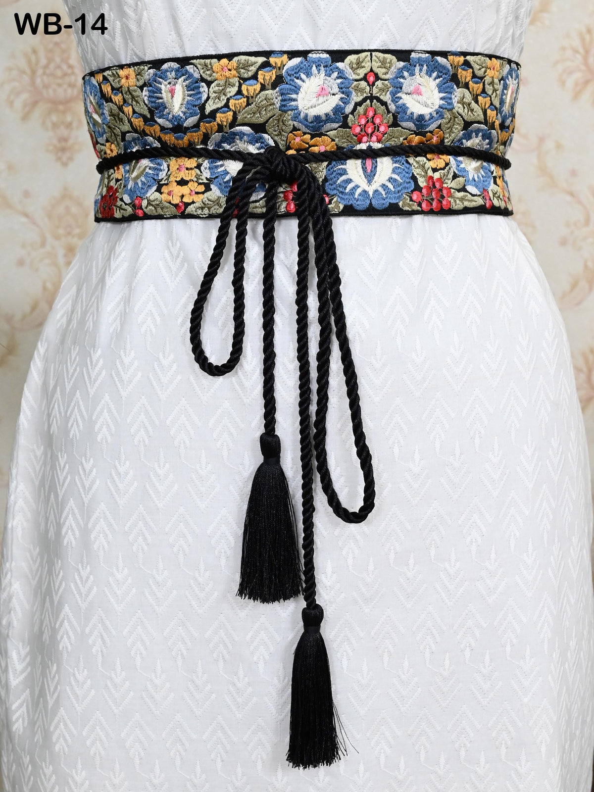 a close-up view of a person wearing a white dress with a decorative belt featuring a floral pattern and a black tassel.