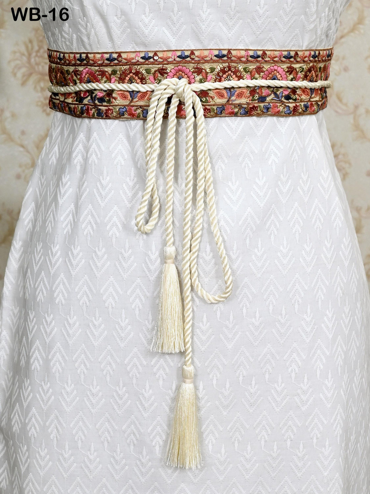 a white dress with a decorative belt featuring a floral pattern and tassels.