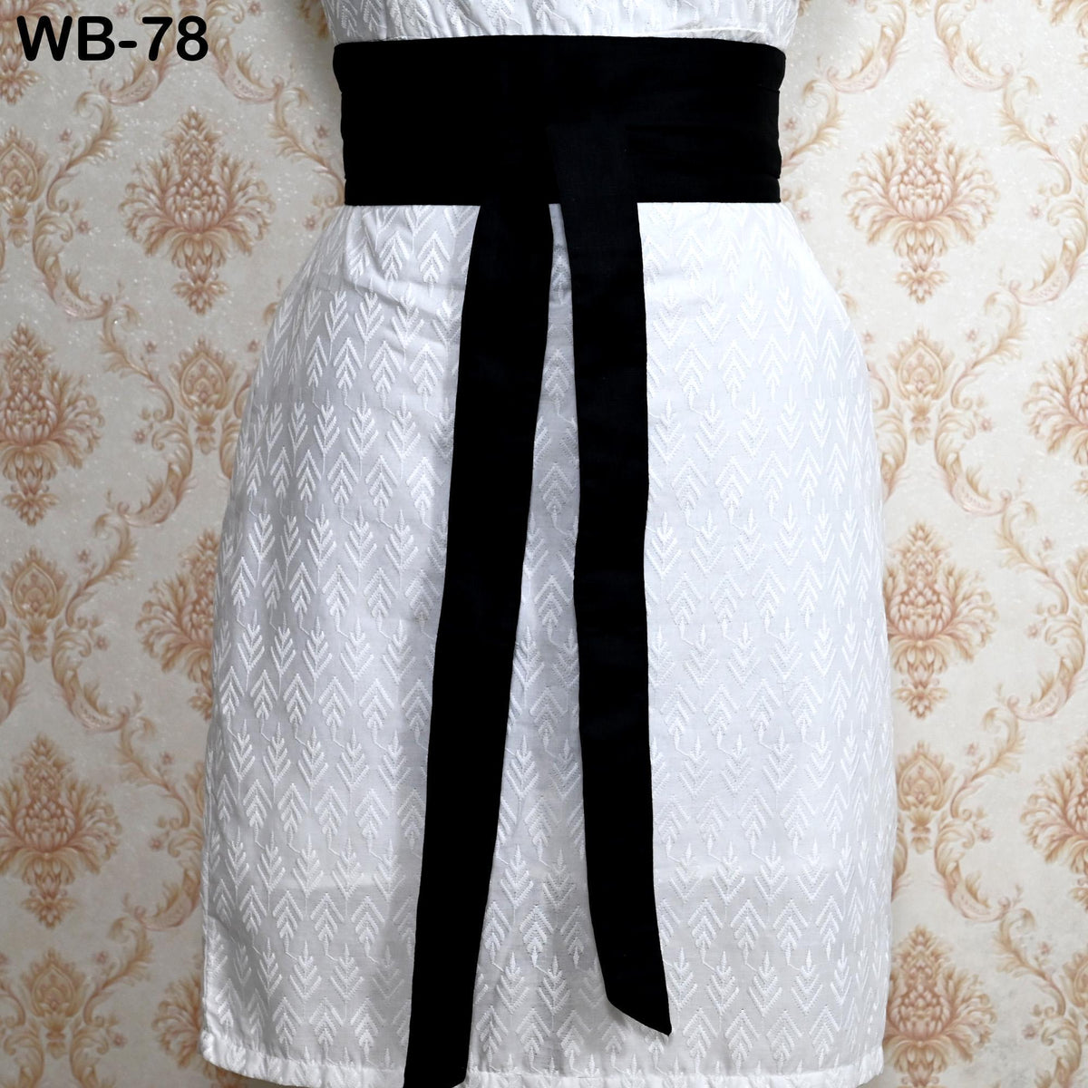 A white dress with a black belt, displayed against a patterned wallpaper background.