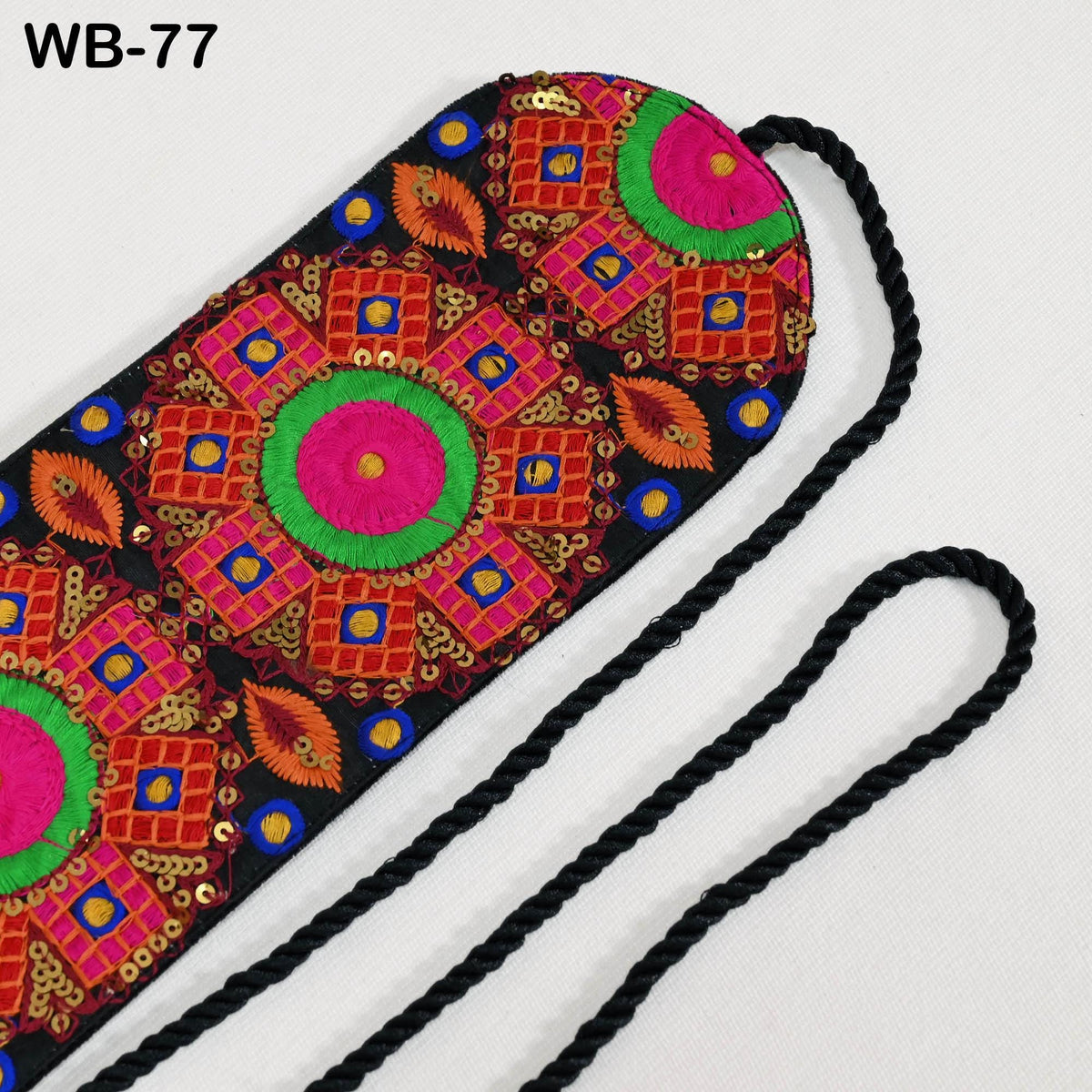 a colorful, intricately embroidered fabric with a geometric pattern in shades of pink, green, and orange. The fabric appears to be a decorative piece, possibly a bag or accessory.