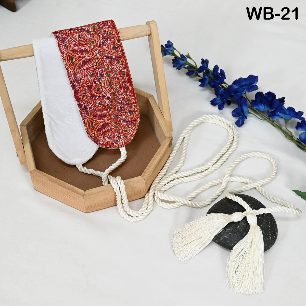 a wooden box with a red and white patterned cloth hanging from it, a white tassel, a black rock, and some blue flowers.