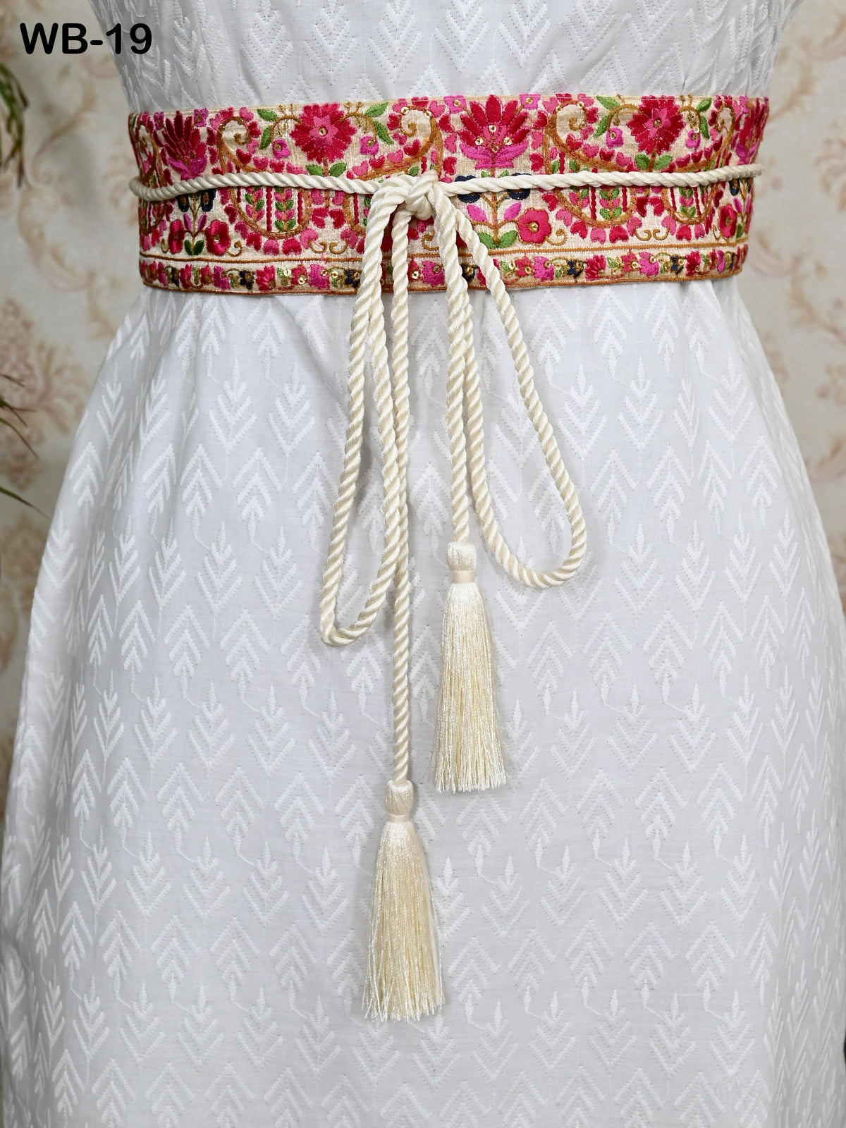 a white dress with a decorative floral belt and tassels.