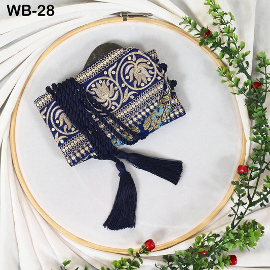 a blue and gold embroidered bag with tassels, placed on a white surface within a wooden frame. The frame is surrounded by greenery, creating a decorative and elegant setting.
