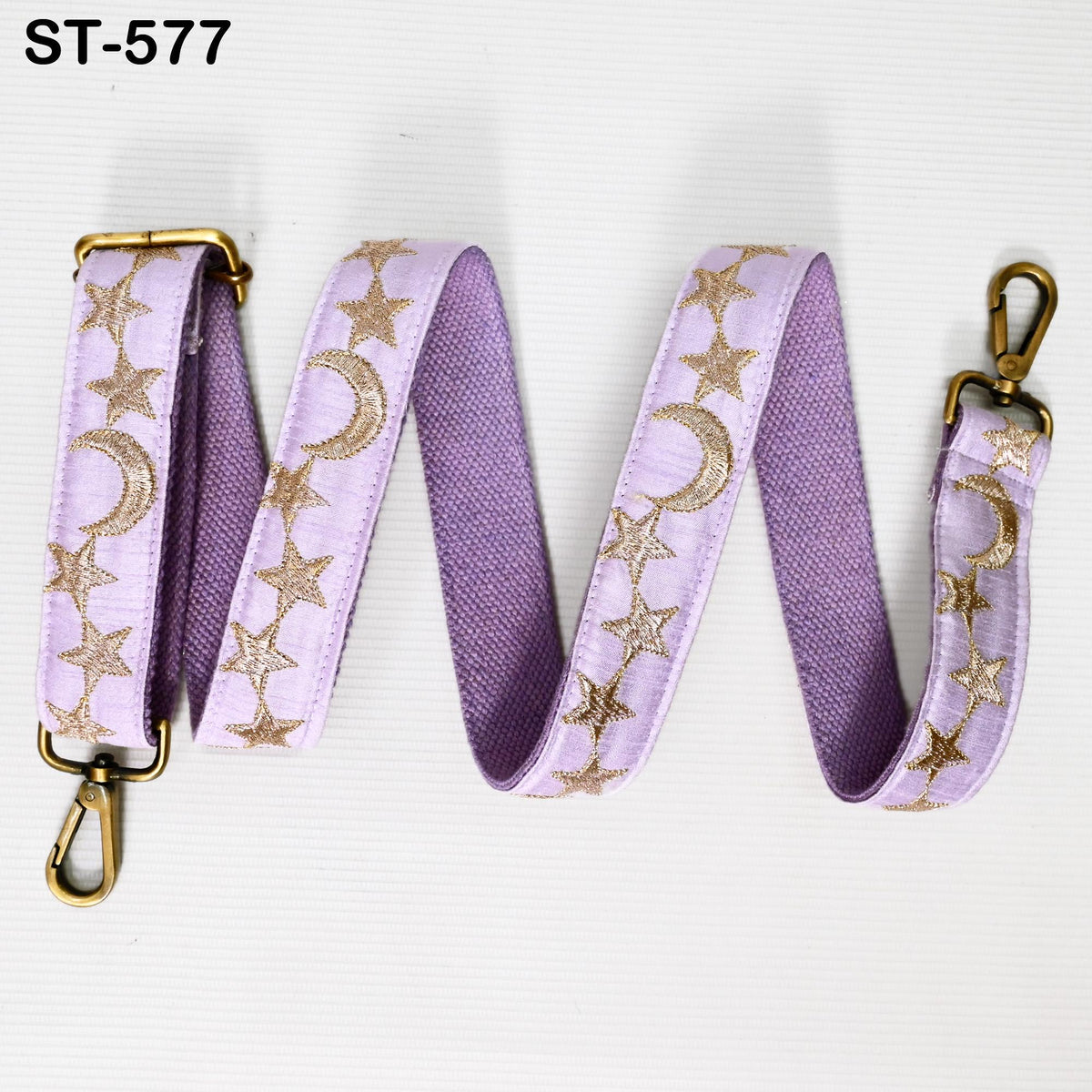 A purple strap with gold stars and crescent moons, attached to a metal clasp, is shown against a white background.