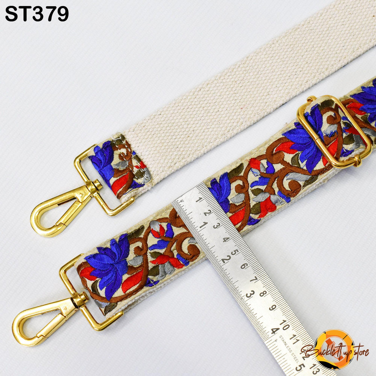 a strap with a floral pattern and two gold metal hooks, with a ruler placed next to it to measure the strap's length.