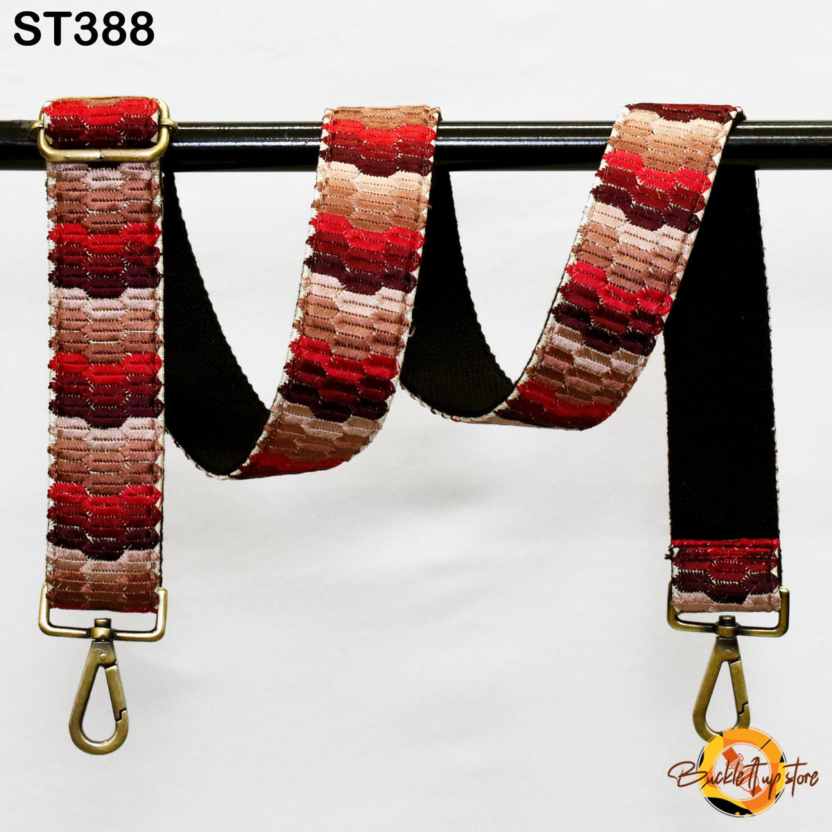 A colorful, patterned strap with a black metal buckle attached to a black metal hook, hanging against a white background.
