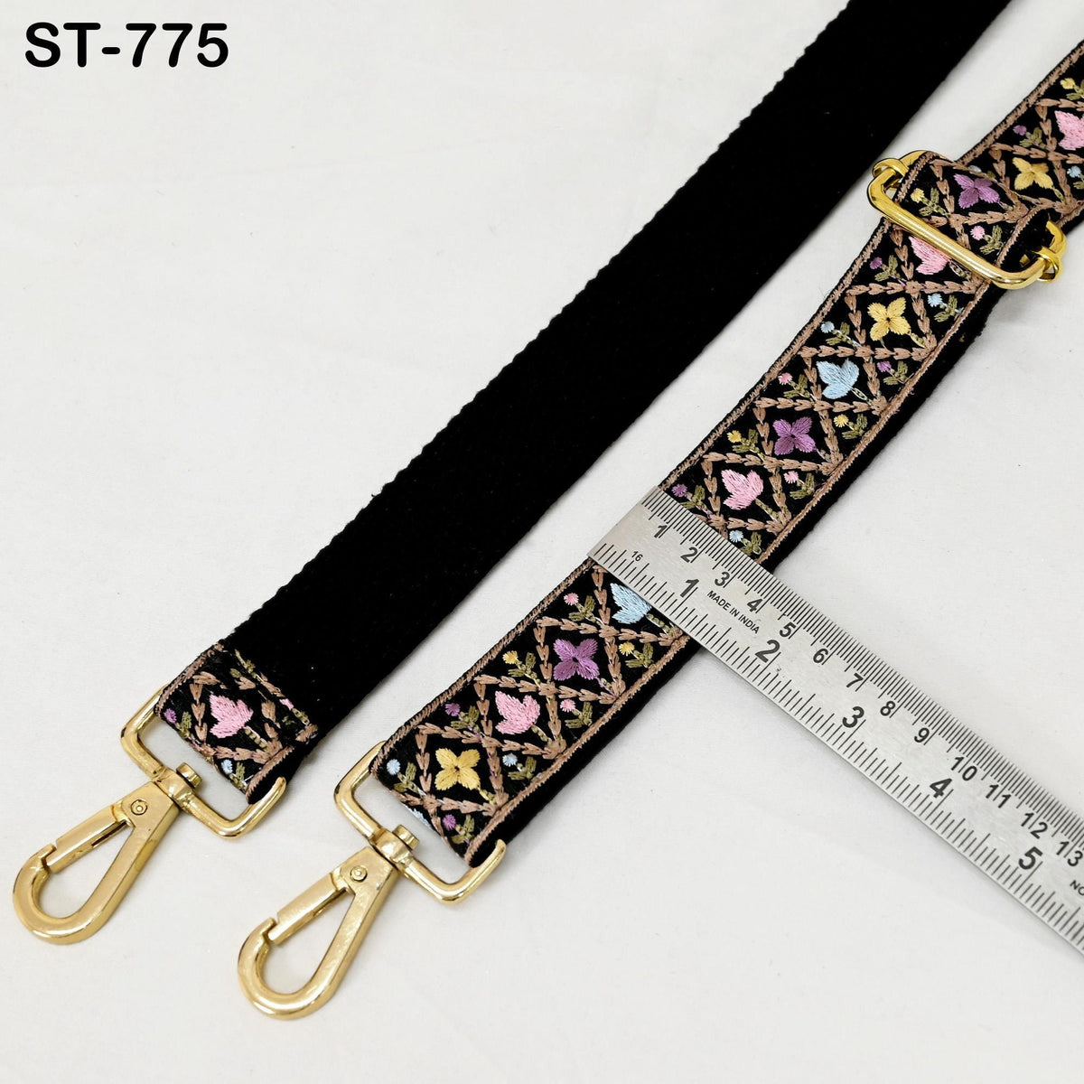 a black strap with a colorful floral pattern and two gold metal hooks, placed next to a ruler for size comparison.