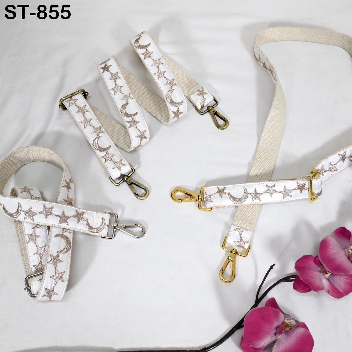 a collection of white straps adorned with star and moon patterns, arranged on a white background. The straps are accompanied by a few pink flowers, adding a touch of color to the scene.