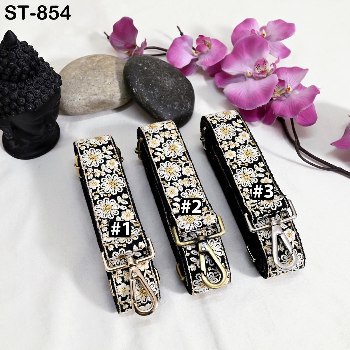 three black and white floral straps with numbers on them, placed on a white surface alongside some pink flowers and rocks.