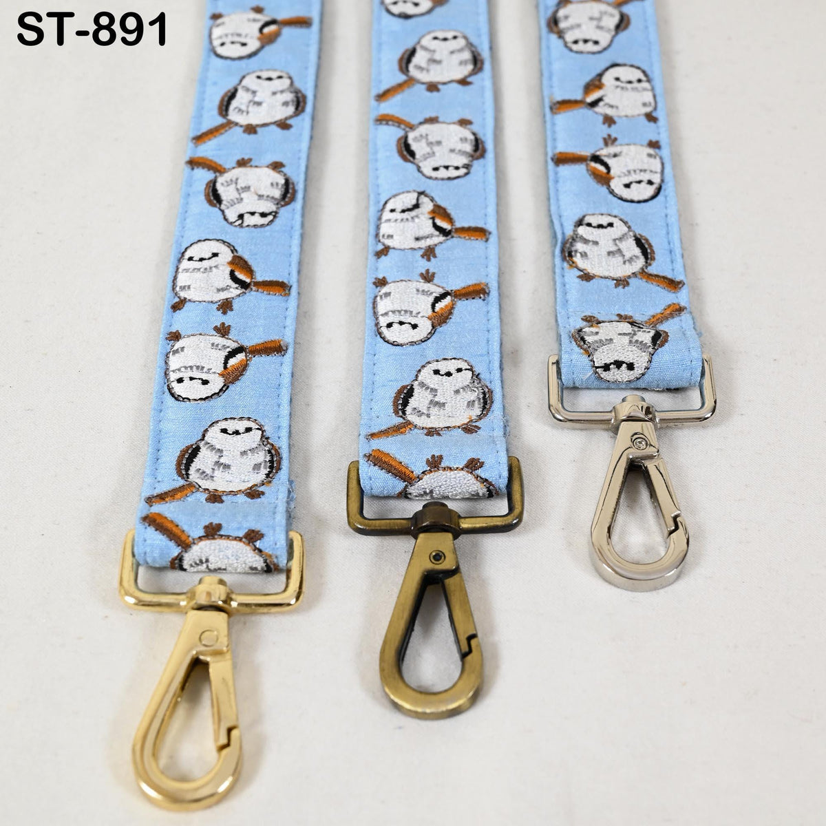 three blue straps with a pattern of small white birds on them, each with a gold metal clasp.