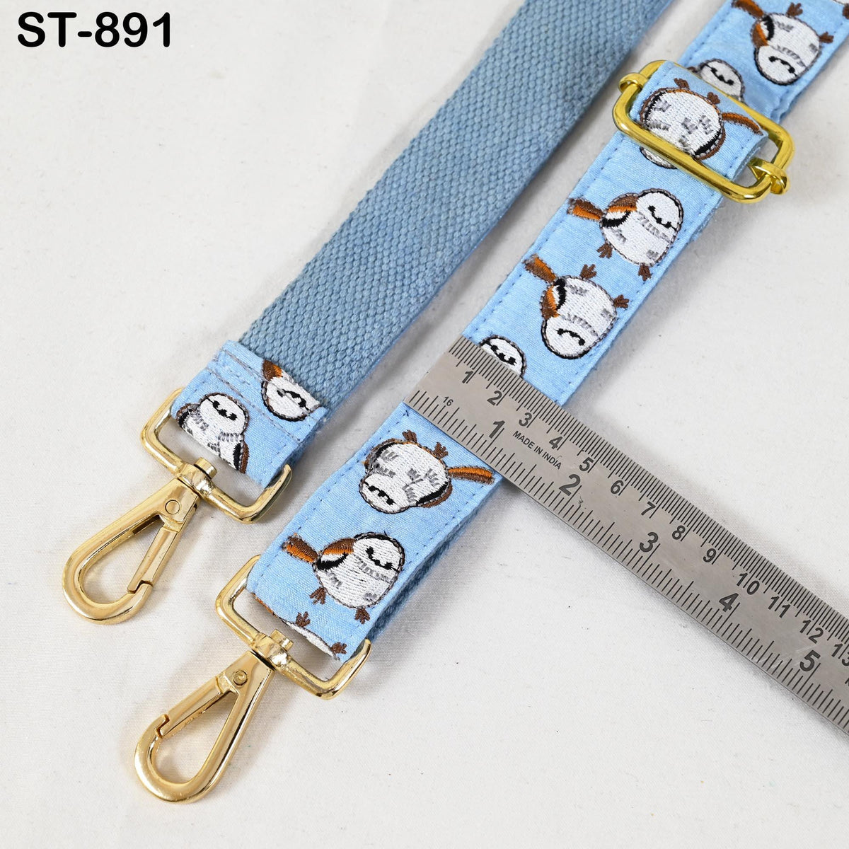 a blue strap with a pattern of small birds printed on it, and a ruler is placed next to it, indicating the strap's length.