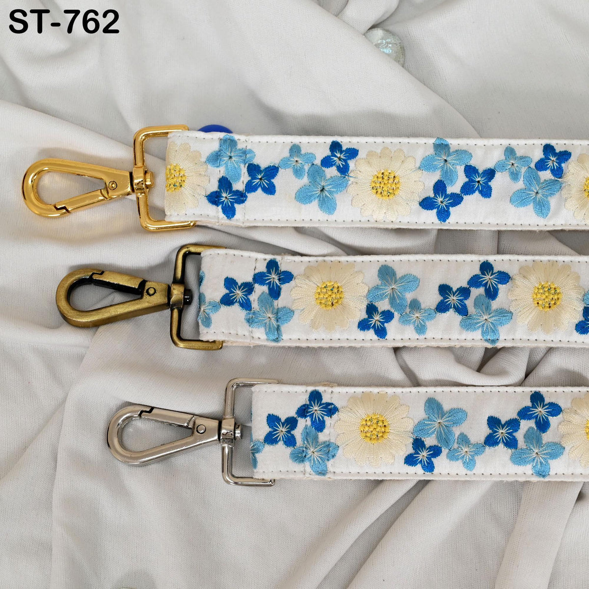 three straps with floral embroidery in blue and white colors. The straps have metal hooks and are arranged in a row on a white background.