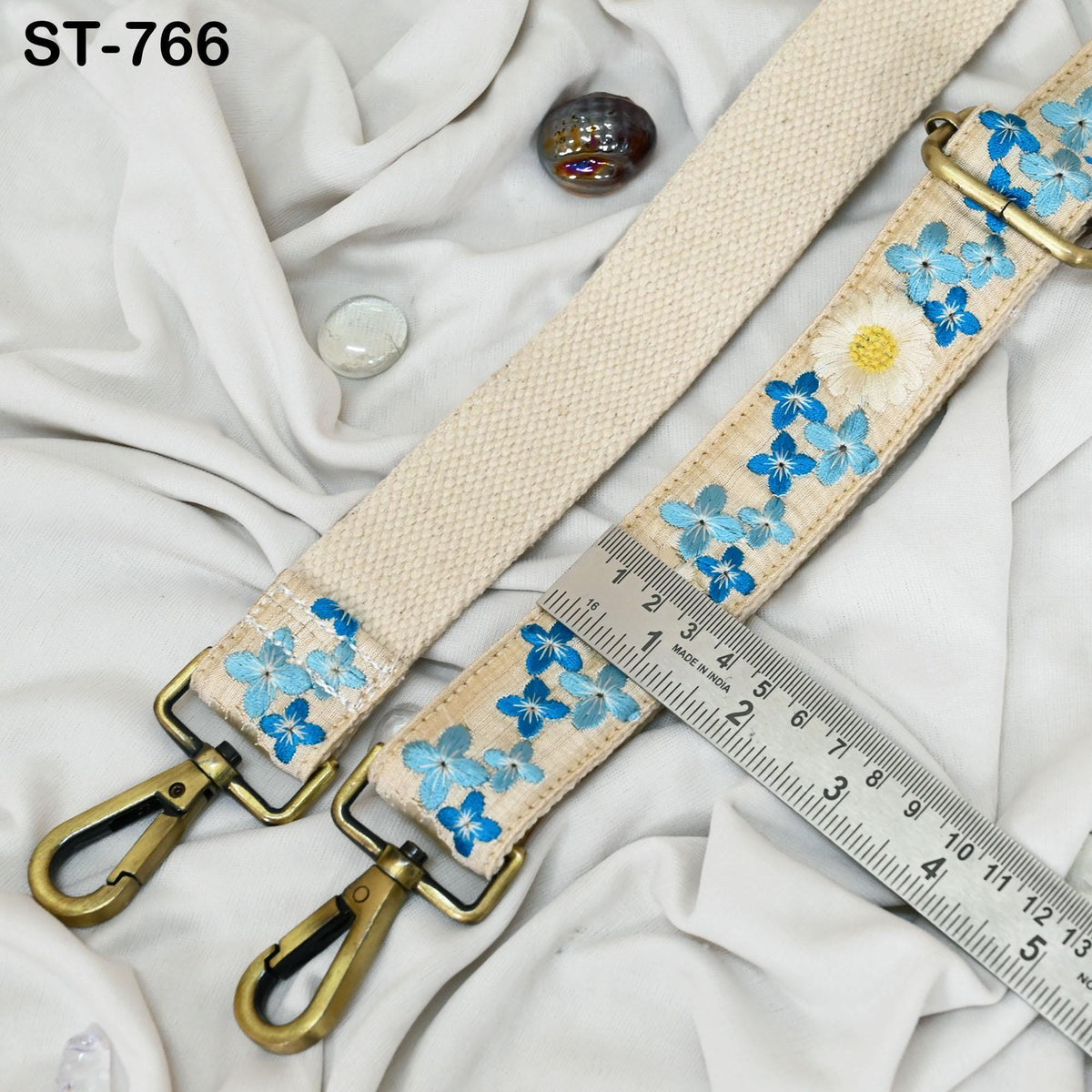 a beige strap with blue floral embroidery, a ruler, and some small objects on a white background.