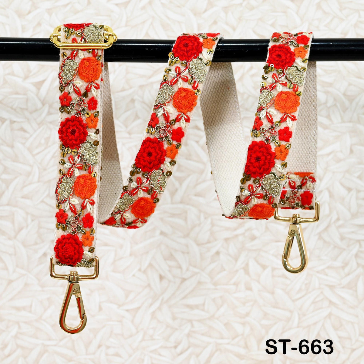 A floral-patterned strap with a gold-colored metal clasp and hook, hanging on a black bar.