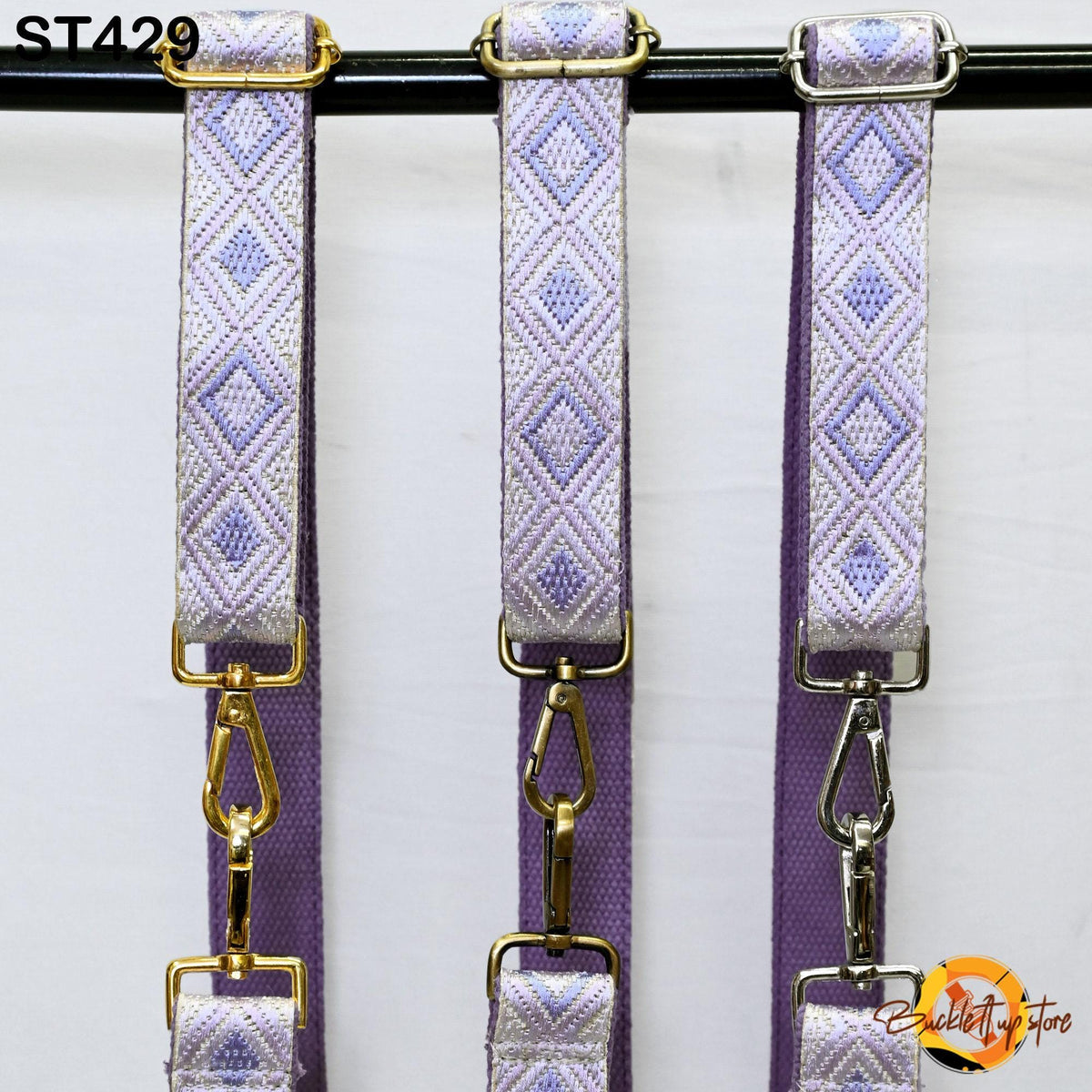 Three purple and gold straps with metal buckles hanging on a black bar.
