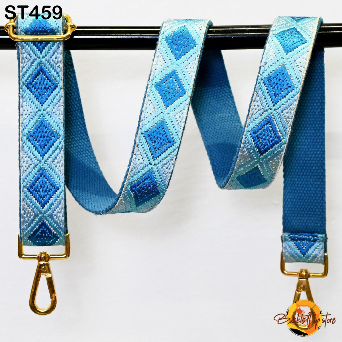 A blue and white patterned strap with a gold metal buckle, hanging on a black bar.