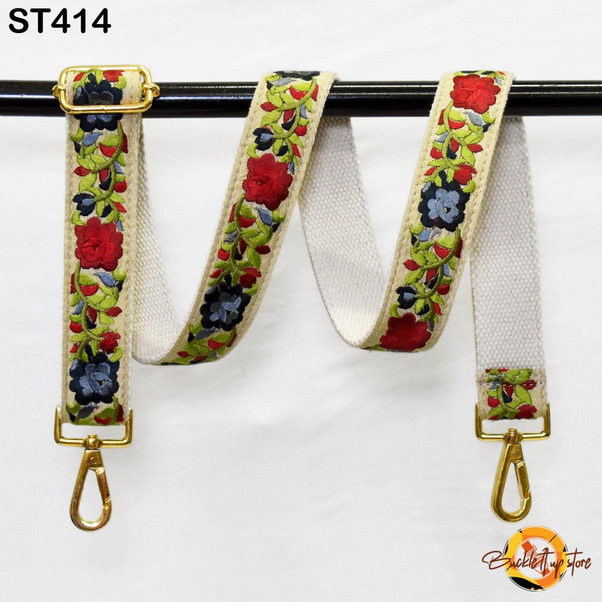 A floral-patterned strap with a gold buckle and two gold hooks, hanging on a black rod.