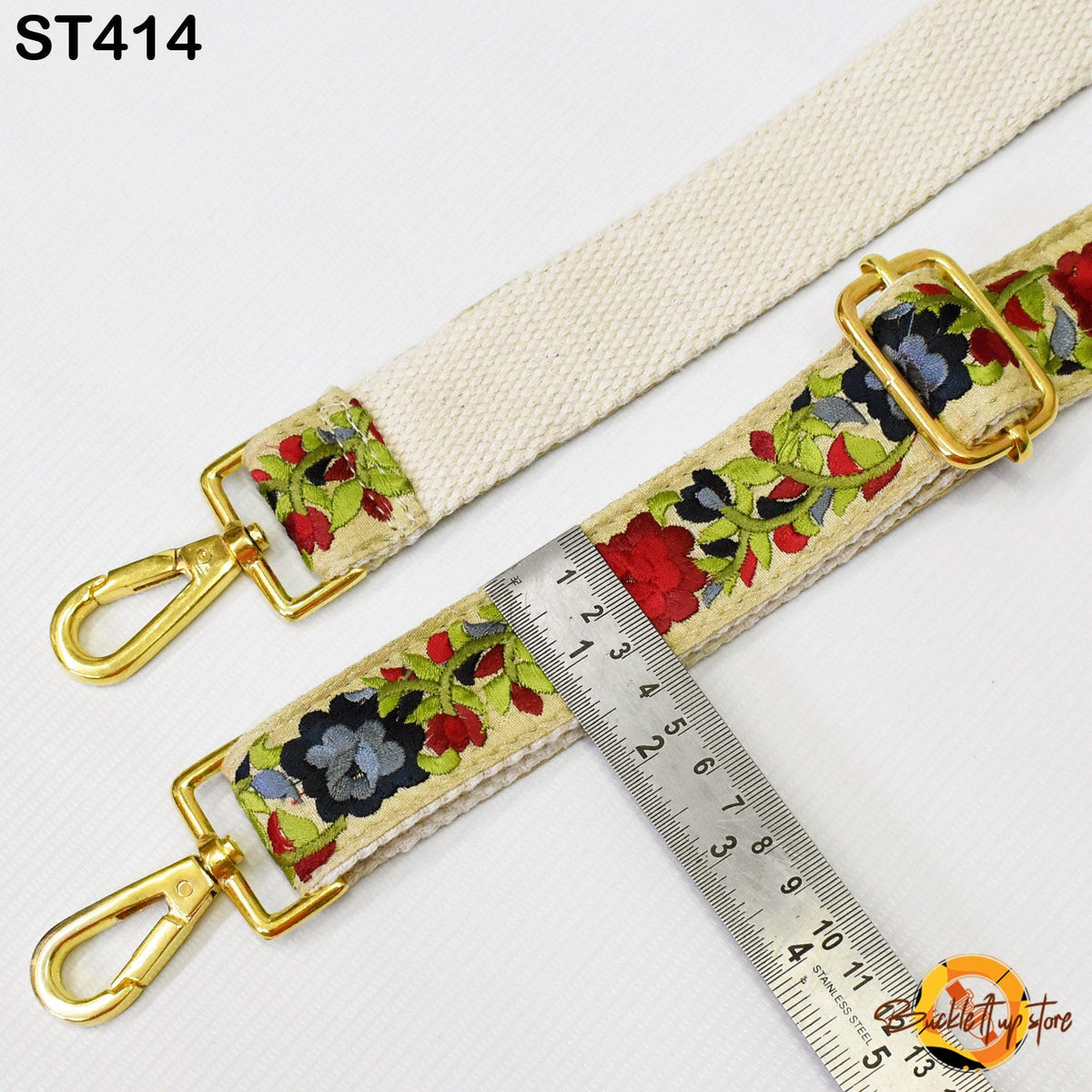 a strap with a floral pattern and two gold-colored metal hooks. A ruler is placed next to the strap, indicating the strap's size.
