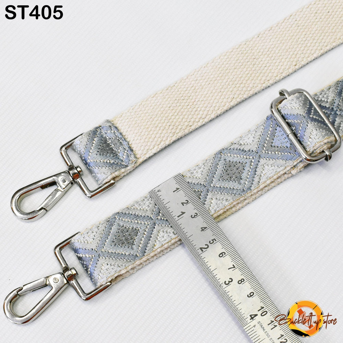 a beige and gray patterned strap with metal hooks, and a ruler is placed next to it, indicating the strap's size.