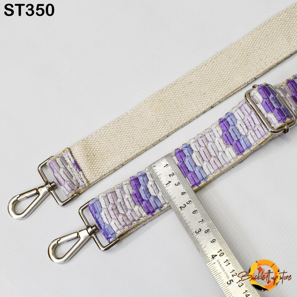a beige strap with a pattern of purple and white, and a metal hook on the end. A ruler is placed next to the strap, indicating the strap's length.