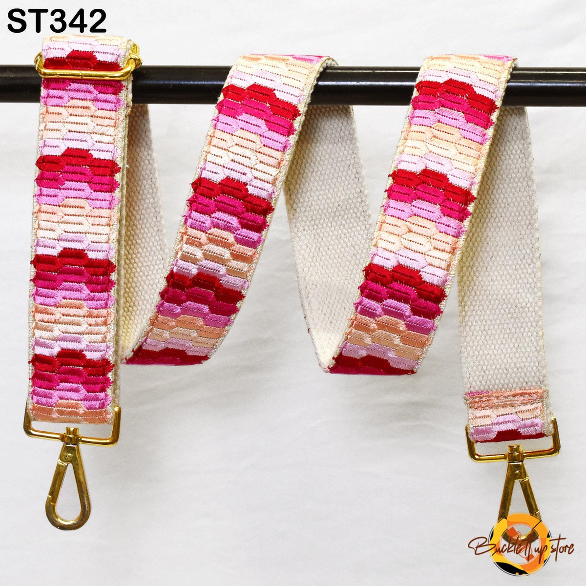 A colorful, patterned strap with a gold buckle is hanging on a black bar.