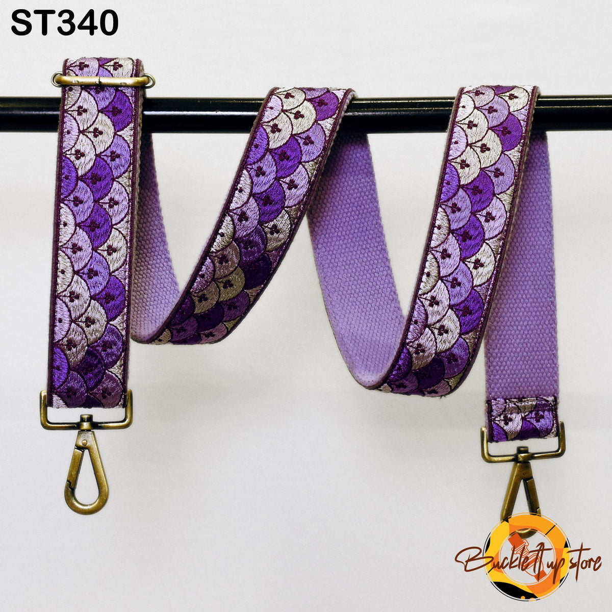 A purple and gold patterned strap with a metal hook attached, hanging on a black bar.