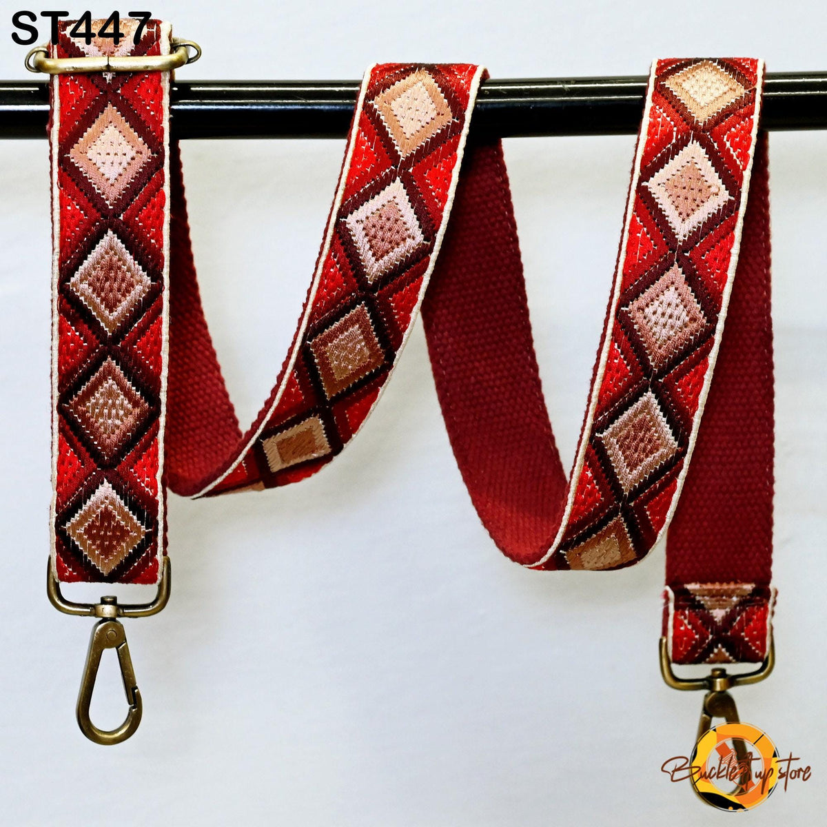 a red and brown patterned strap with a metal clasp, hanging on a black bar.