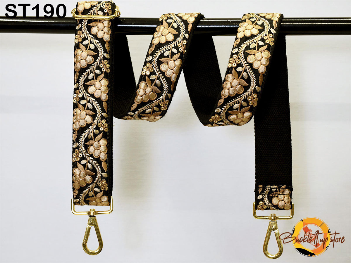 A black and gold floral patterned strap with gold hardware, hanging on a black rod.