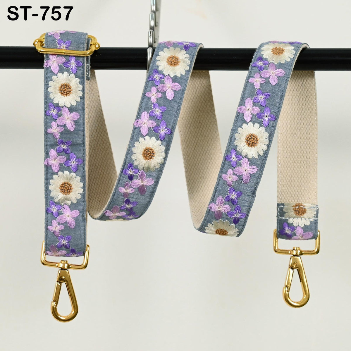 A floral-patterned fabric strap with a gold metal buckle, hanging on a black hook.