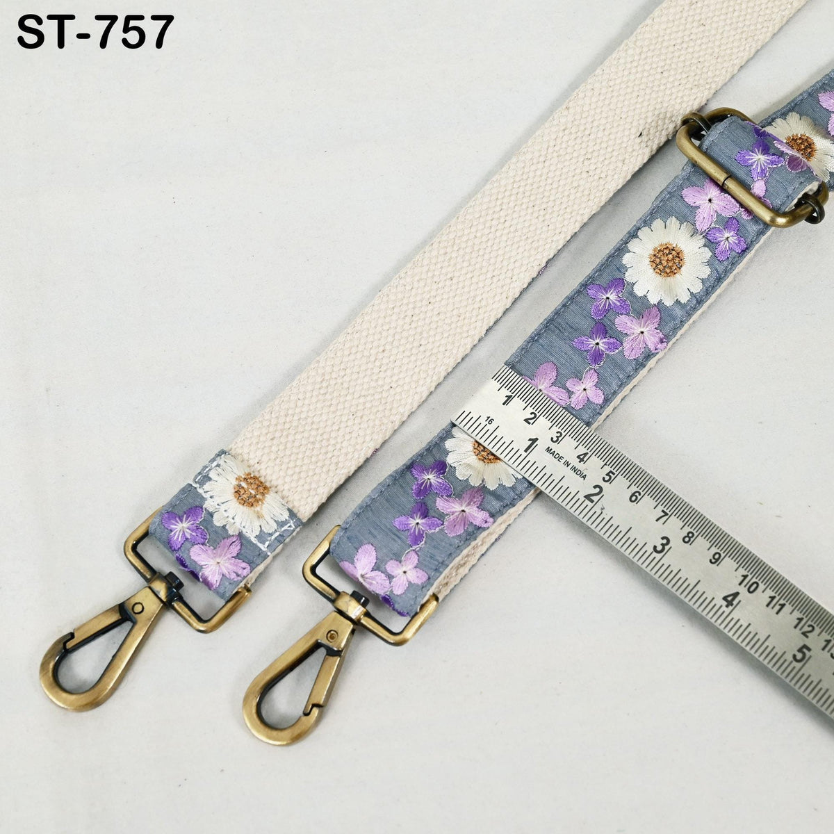 a beige strap with a floral pattern, featuring two metal hooks and a ruler for size comparison.