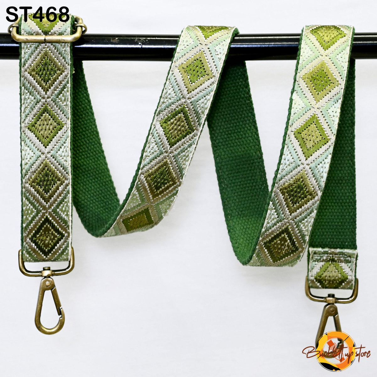 A green and white patterned strap with a metal hook attached, hanging on a black bar.
