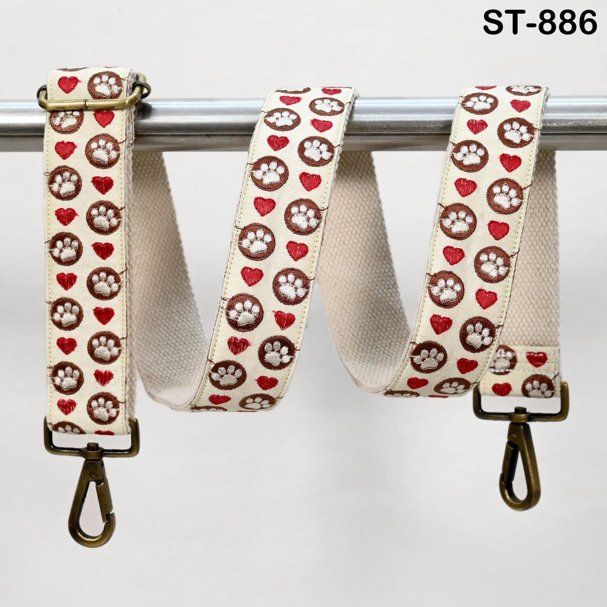 A white strap with a pattern of red hearts and paw prints, hanging from a metal hook.