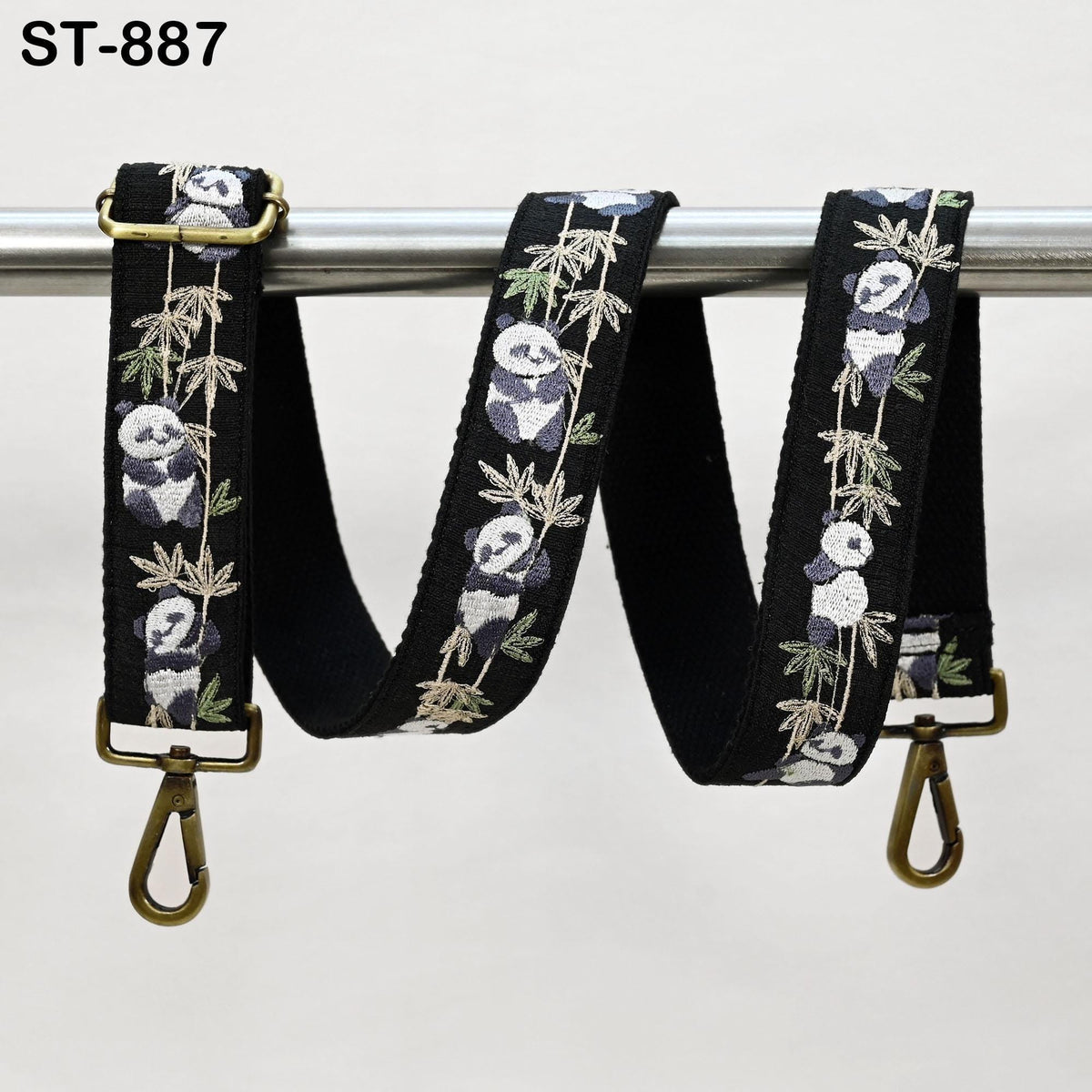 A black strap with a floral pattern of panda bears hanging from a metal bar.