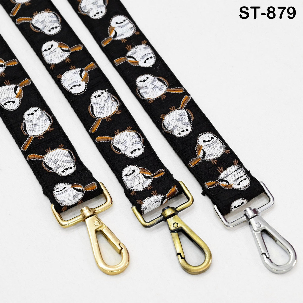 three black straps with gold metal hooks attached to them. The straps have a repeating pattern of small white and orange birds printed on them.