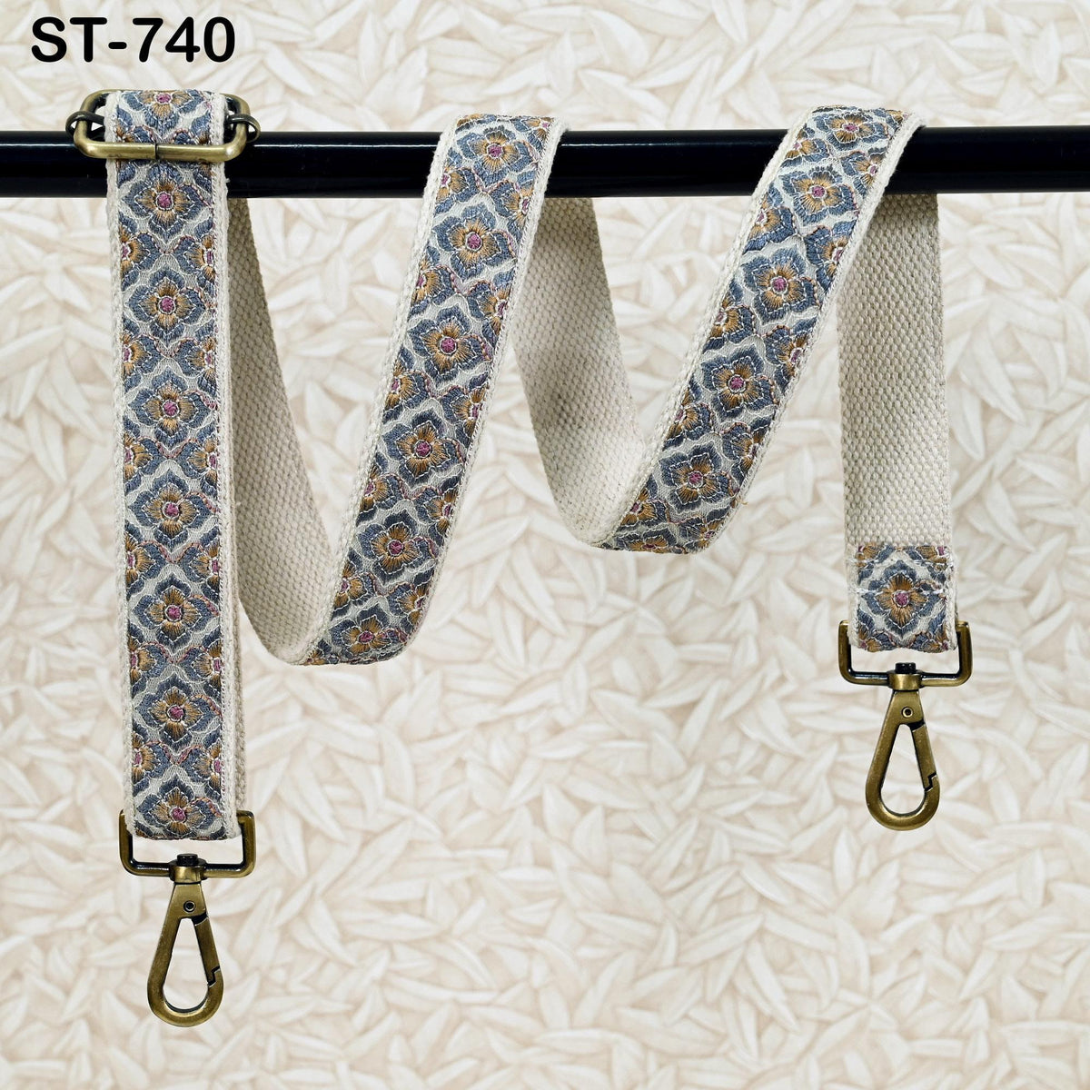 A beige patterned strap with a metal buckle and two metal hooks attached to a black metal bar.