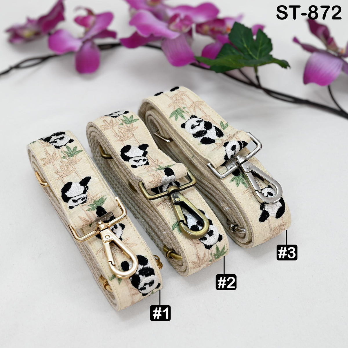 Three beige straps with panda designs, each with a metal clasp and a small tag indicating the number. The straps are arranged on a white surface, with purple flowers in the background.