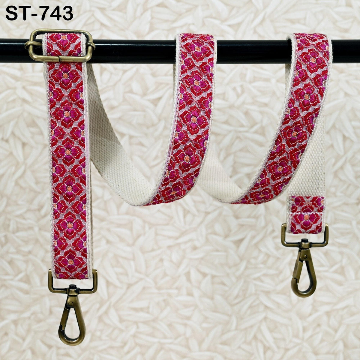 A pair of pink and white patterned straps with metal buckles, hanging from a black bar.