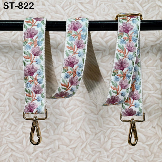 a floral patterned strap with gold metal hooks attached to it, hanging on a black bar.
