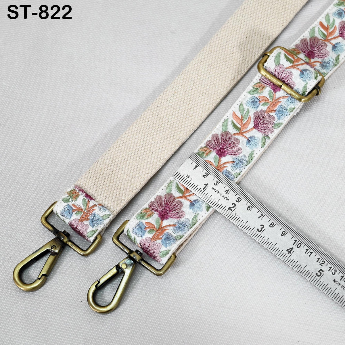 a beige strap with a floral pattern and two metal hooks, one on each end. A ruler is placed next to the strap, indicating the strap's length.